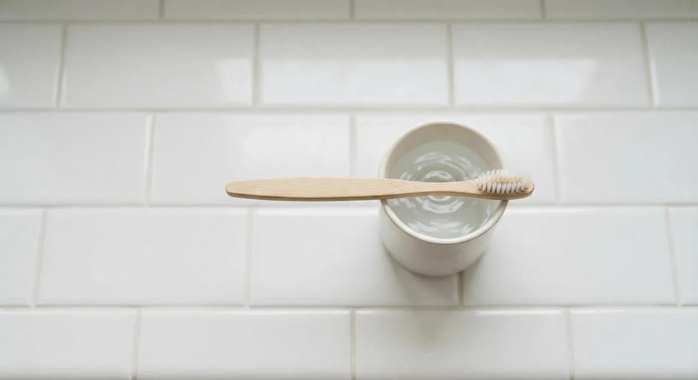 A soft toothbrush resting on a cup of water on white tiles