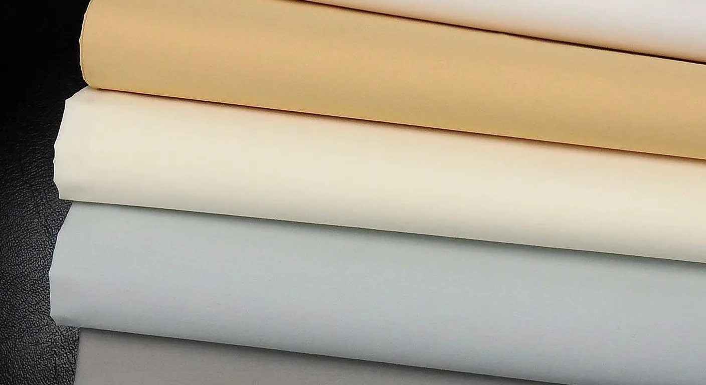 A stack of folded percale sheets in grey, white, cream and gold