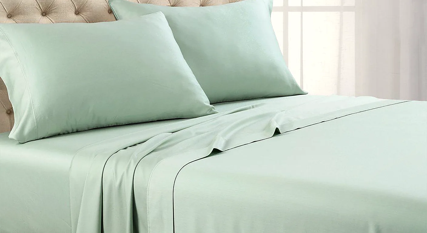 A bed made up with sea-green eucalyptus TENCEL lyocell sheets and pillowcases